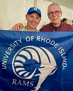 Michael Dunlap and Rick Rhodes holding up a banner with the URI rams logo