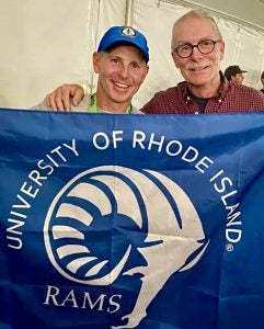 Michael Dunlap and Rick Rhodes holding up a banner with the URI rams logo