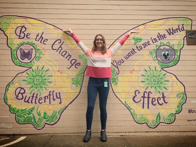 Taylor Booth standing in front of a butterfly selfie spot painted onto a building