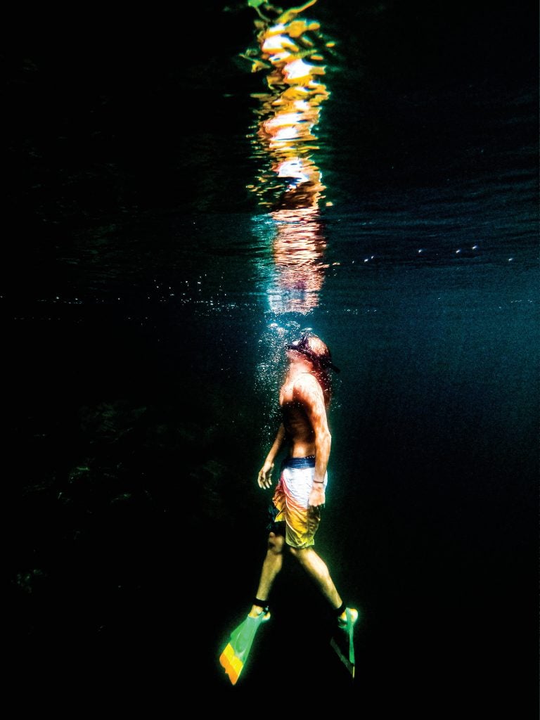 A diver swimming up towards the surface in a dark body of water.