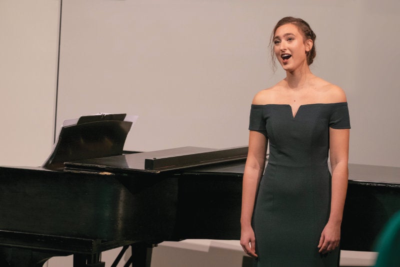 Elise Felker singing next to a piano