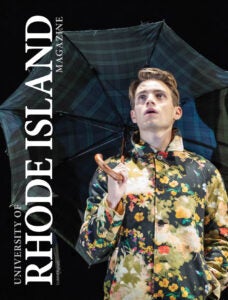 University of Rhode Island Magazine Cover featuring Tony Award-Winning Actor Andrew Burnap ’13 holding an umbrella on stage in the Inheritance