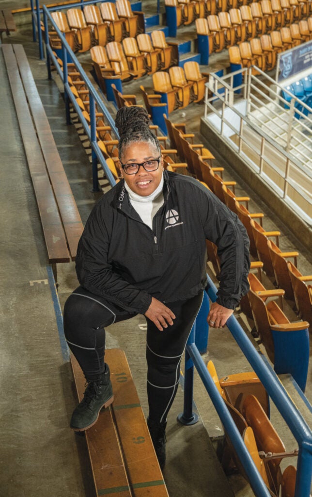 URI basketball star Tracey Hathaway ’86 standing in a basketball arena in the bleachers