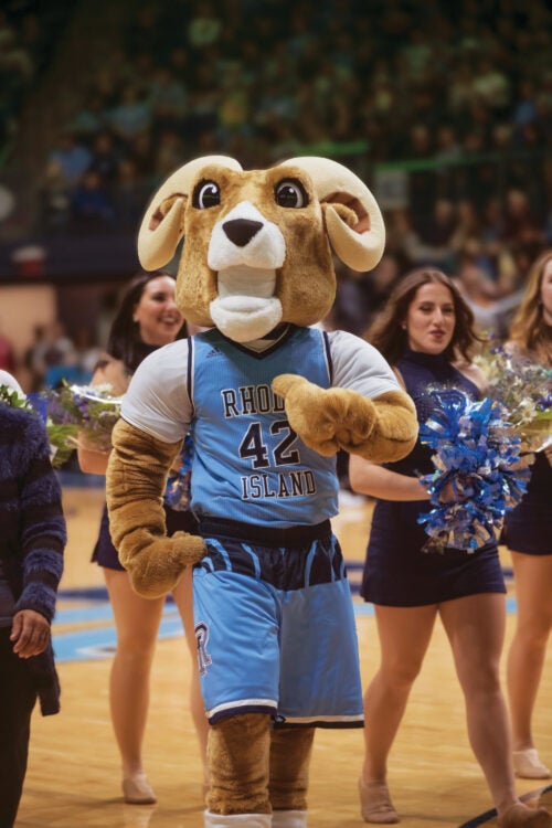 Rhody the Ram, standing in front of cheerleaders, cheering the Men's URI basketball team during the game