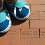 Rhody's feet beside a commemorative brick on the century walk that reads: 2 Rams in Love