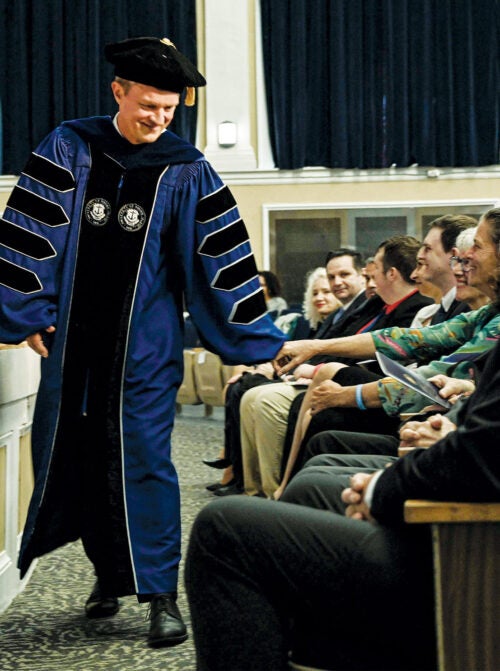 President Parlange with his arm outstretched at a commencement ceremony
