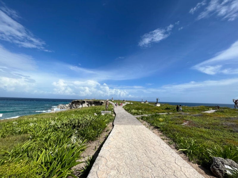 A paved pathway on an oceanfront peninsula winding past sculptures