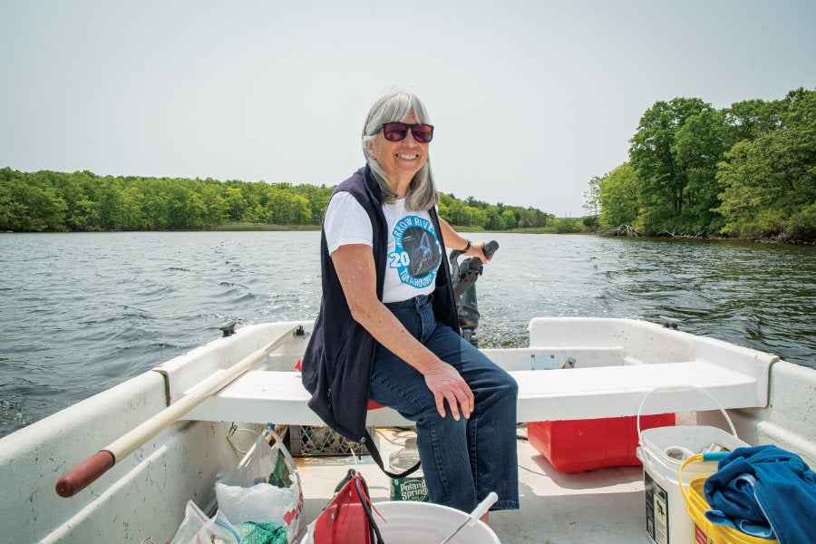 Veronica Berounsky, Ph.D. ’90 sitting in the stern of a boat, driving an outboard motor, on Narrow River