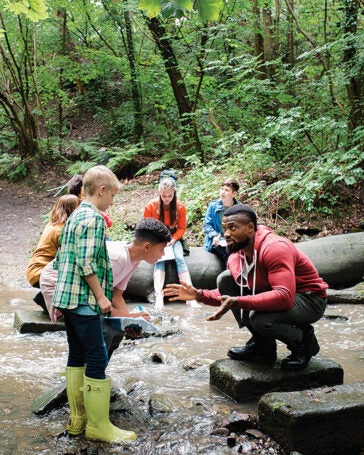 young man working with a group of children outside by a flowing stream