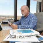 URI economics professor Leonard Lardaro sitting at his desk looking down at a piece of paper