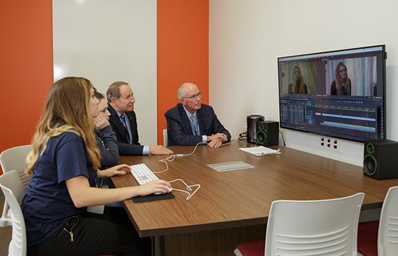 A QUICK LEARNING SESSION: From left, URI Harington School students, Devyn Branick and Brianna Creech, show URI President David M. Dooley and Richard J. Harrington, ‘73, Hon. ’02, chairman and general partner of Cue Ball, a venture capital firm, and former president and chief executive officer of the Thomson Reuters Corp., the new technology in the Harrington Hub. URI photos by Jessica Vescera