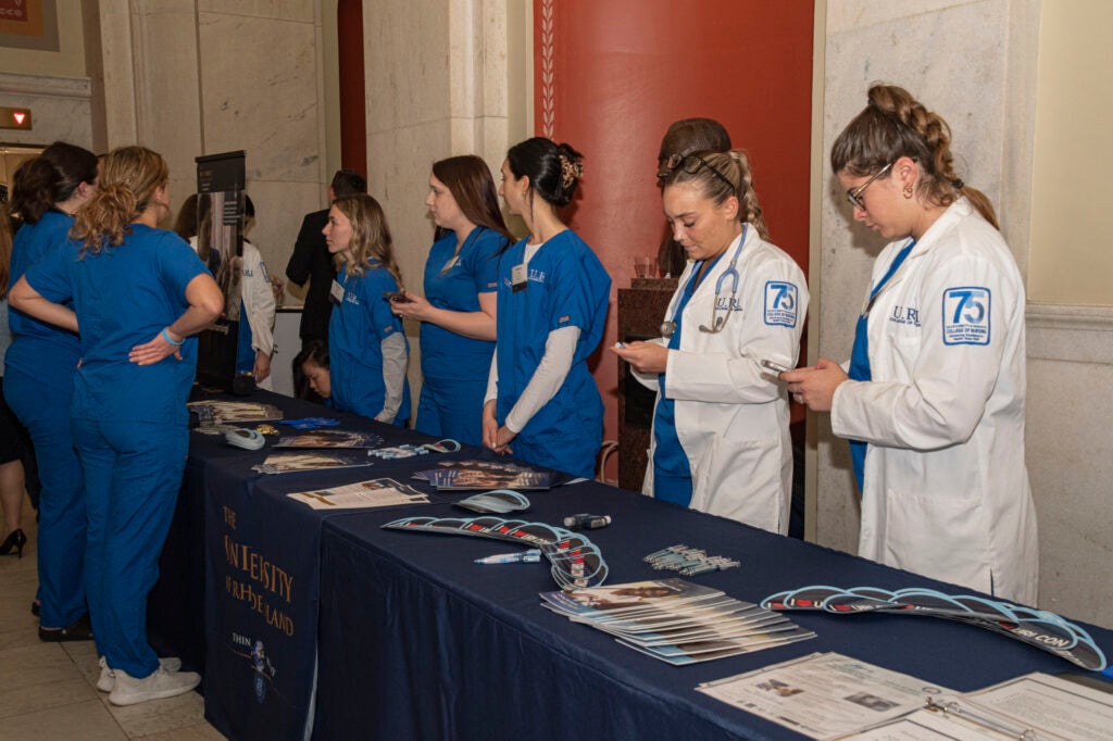 Students of the URI nursing program stand behind a long table