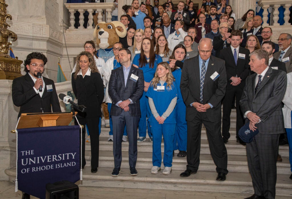 A large gathering of people stand on steps leading down to a podium, where a man is speaking