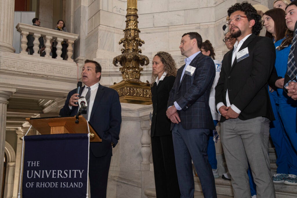 People gathered behind a podium while a man speaks with a microphone