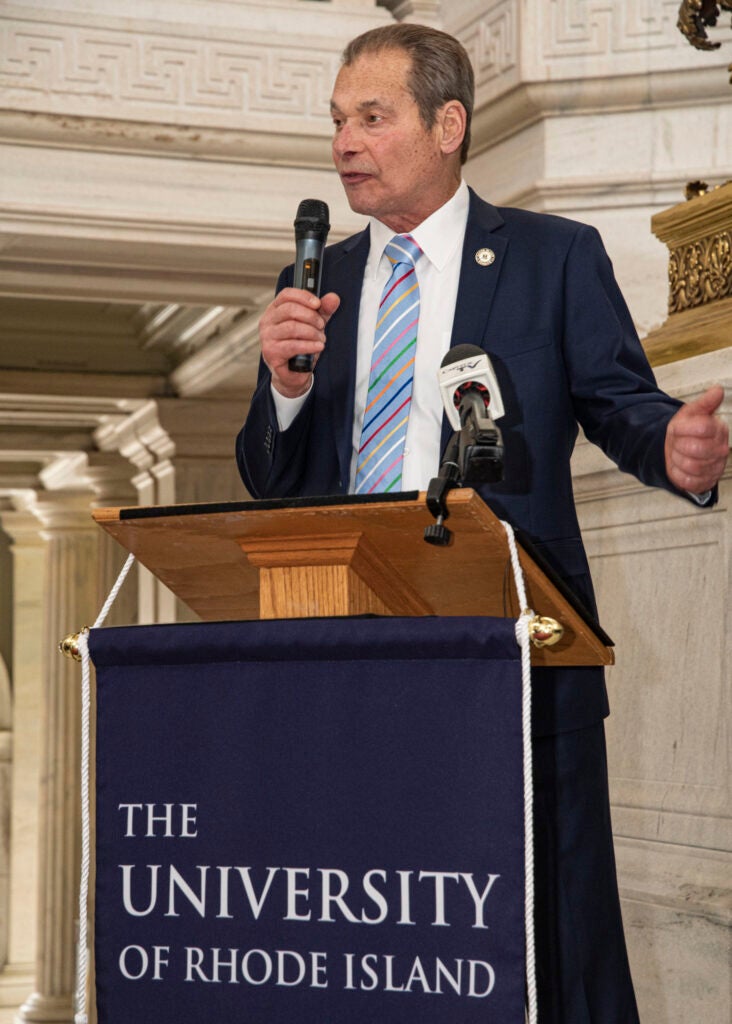 A man speaks holding a microphone while standing behind a podium