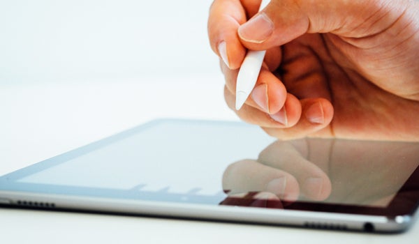 A hand holding a stylus, on top of a tablet