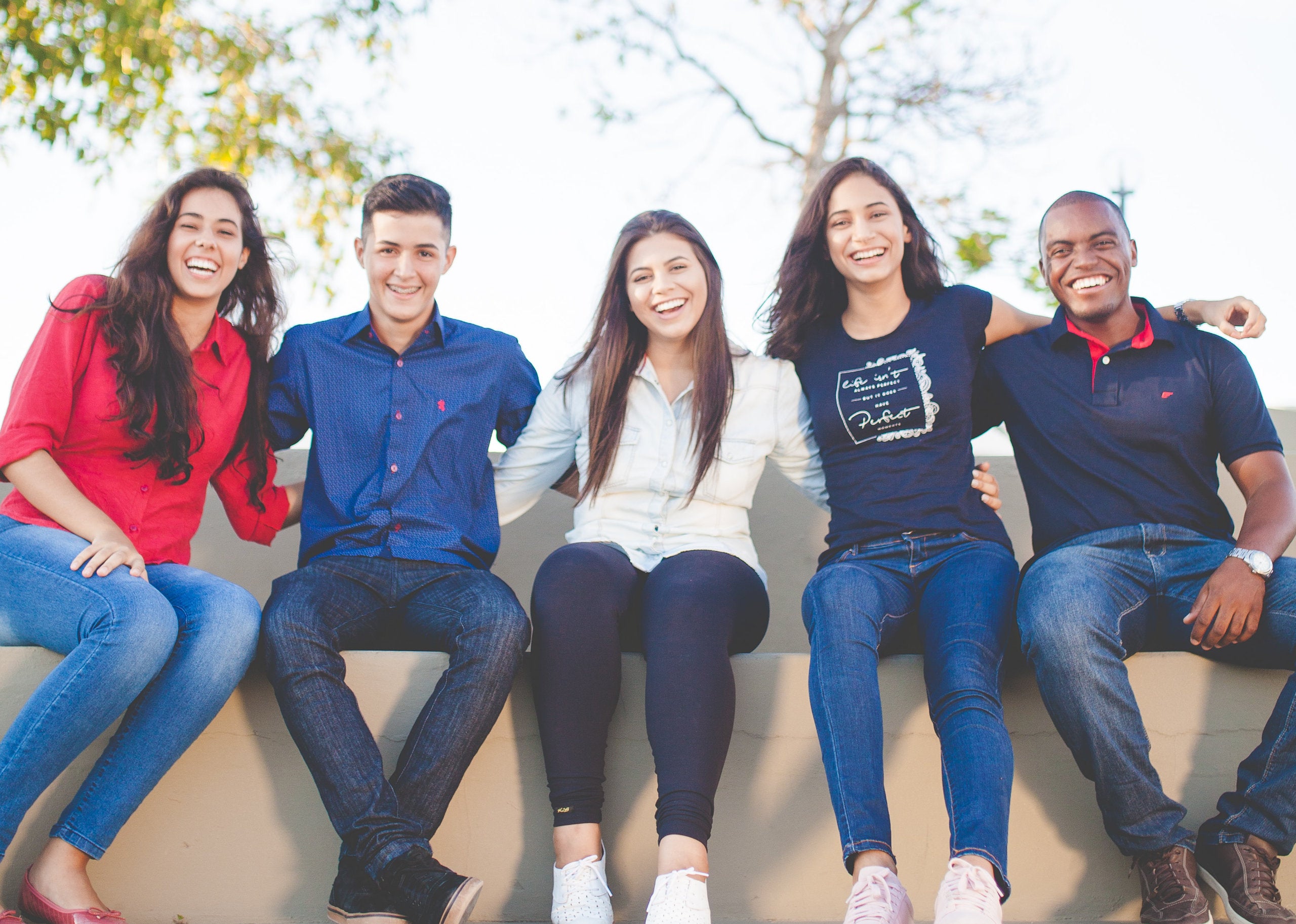 College students sit together on a wall and smile at the camera