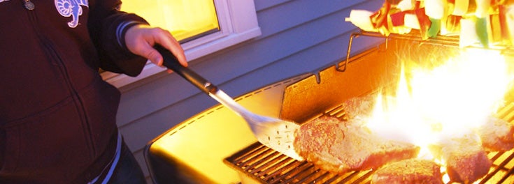 Person grilling steak on a barbecue grill