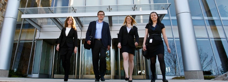 Four URI MBA students dressed in suits walking out of the Fidelity building toward the camera.