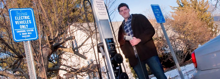 URI student standing next to electric car fueling station URI student standing next to electric car fueling station