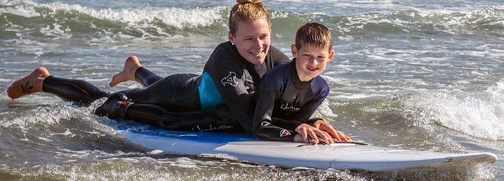 Kinesiology grad student practicing surf therapy with child at Narragansett beach