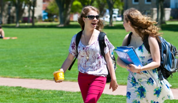 Two women wearing summer clothes, walking across the Kingston Campus in South Kingstown.