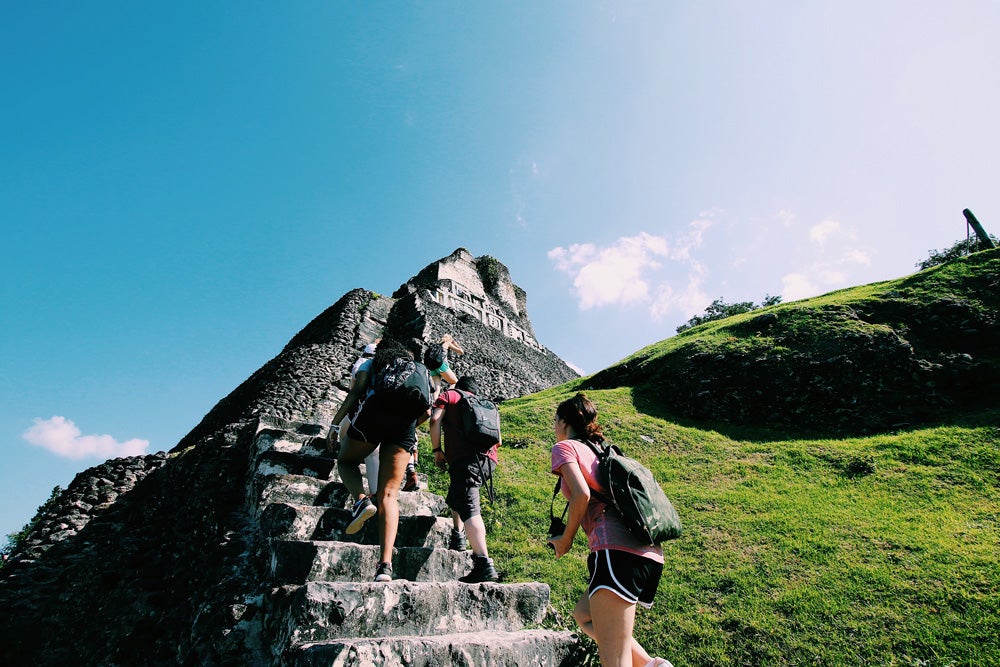URI students participating in a J-term trip to Belize walk up the large stone staircase to the top of the Mayan ruins