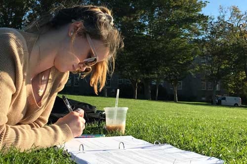girl writing in a notebook on the quad
