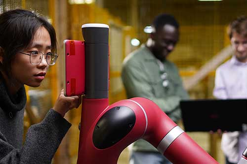 A team of engineering students work with a robotic arm