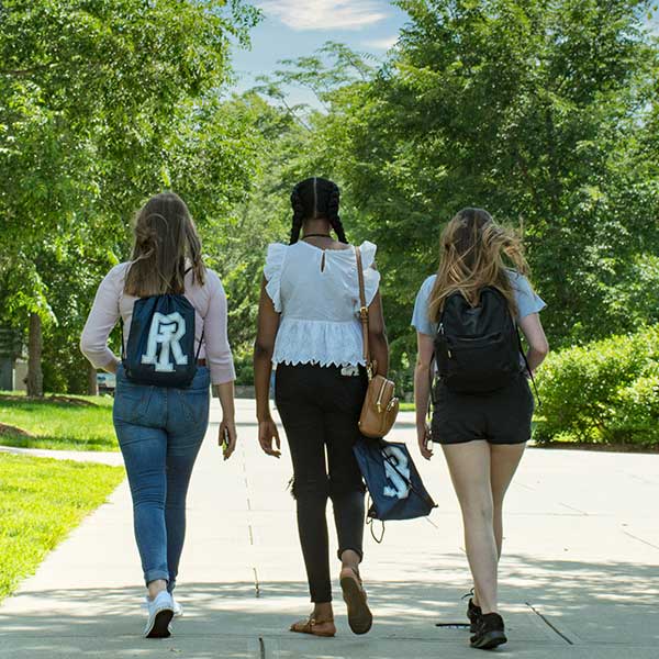 Three students walking on campus in spring (back view)