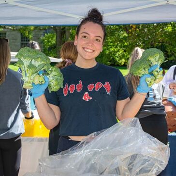 Student volunteer at URI Free Farmers' Market with freshly harvested broccoli