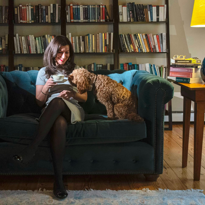 English professor Sarah Eron sitting on a sofa with her dog in front of a wall of bookshelves 