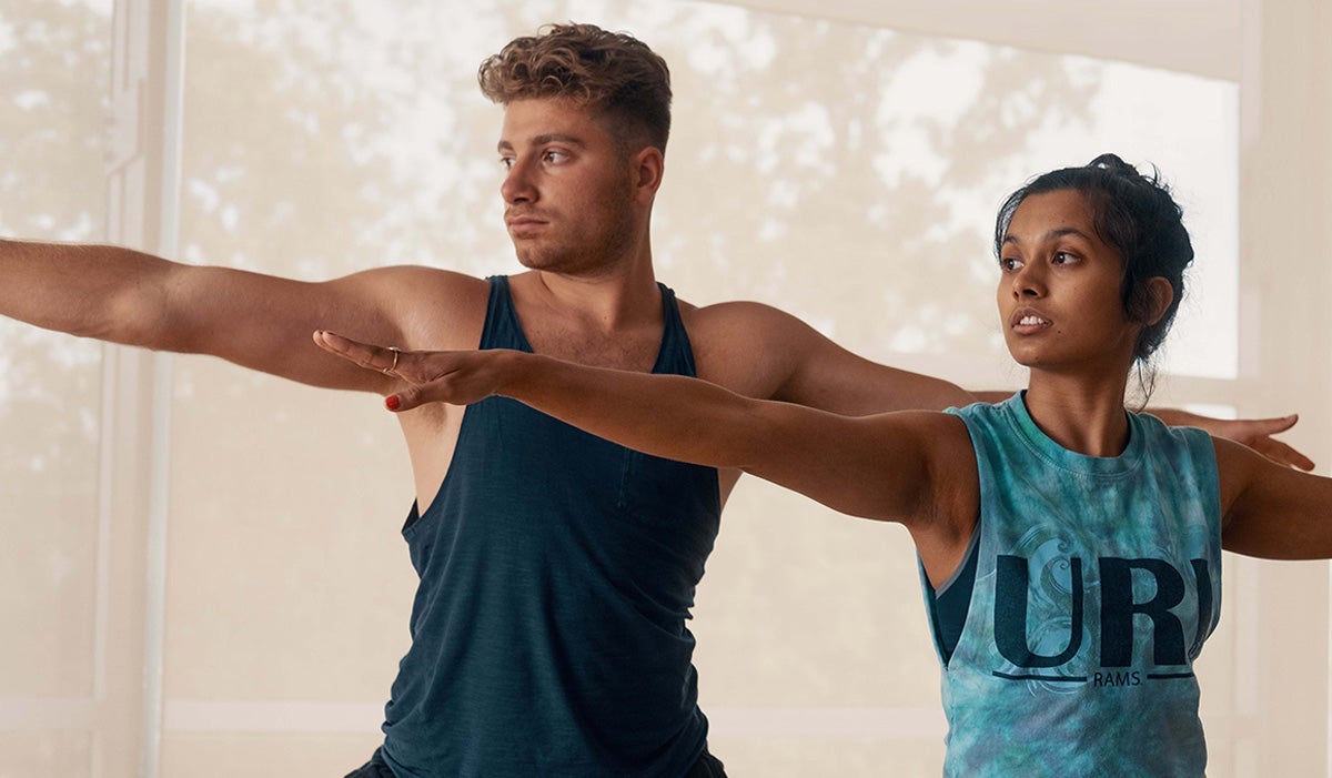 male and female practicing yoga and standing in warrior pose